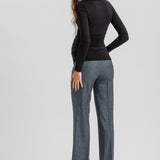 A woman shown from the back wearing a fitted black long-sleeve top, wide-leg charcoal gray trousers, and black high heels against a light gray studio background.
