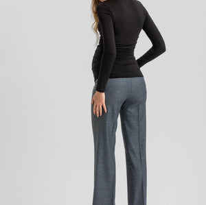 A woman shown from the back wearing a fitted black long-sleeve top, wide-leg charcoal gray trousers, and black high heels against a light gray studio background.