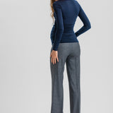 A woman shown from the back wearing a fitted navy long-sleeve top, gray wide-leg trousers, and black heels against a light gray studio background.