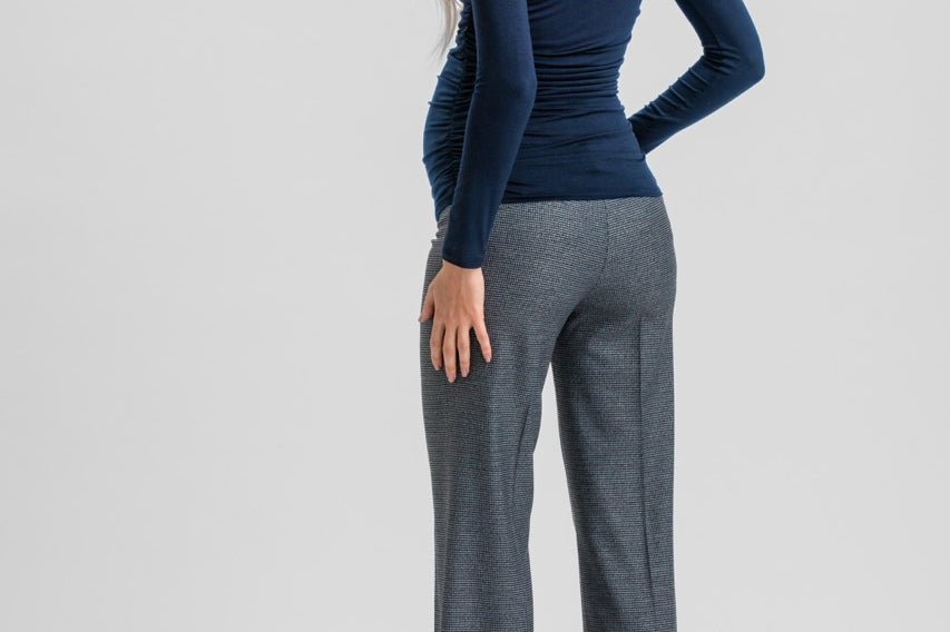 A woman shown from the back wearing a fitted navy long-sleeve top, gray wide-leg trousers, and black heels against a light gray studio background.