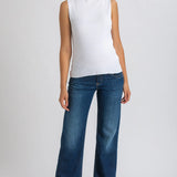Woman wearing white top and dark blue wide leg maternity jeans on white background