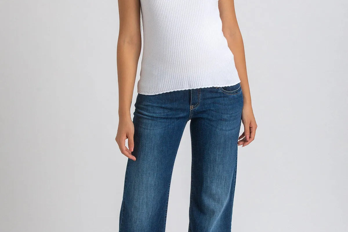 Woman wearing white top and dark blue wide leg maternity jeans on white background