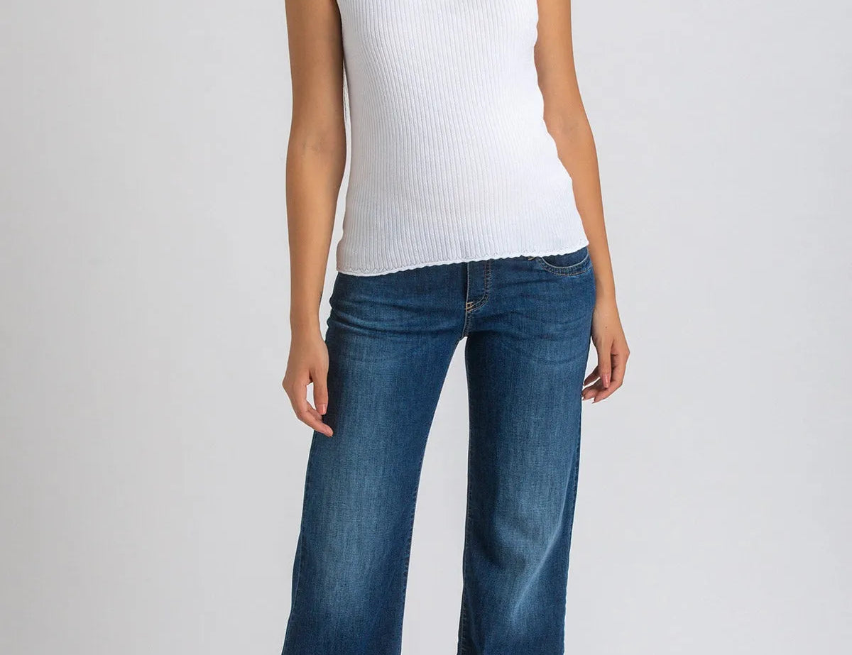 Woman wearing white top and dark blue wide leg maternity jeans on white background