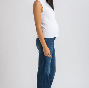 Woman wearing a white sleeveless top and blue jeans on a plain background