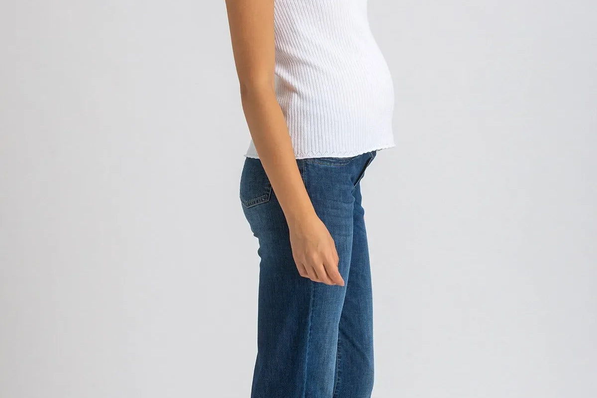 Woman wearing a white sleeveless top and blue jeans on a plain background