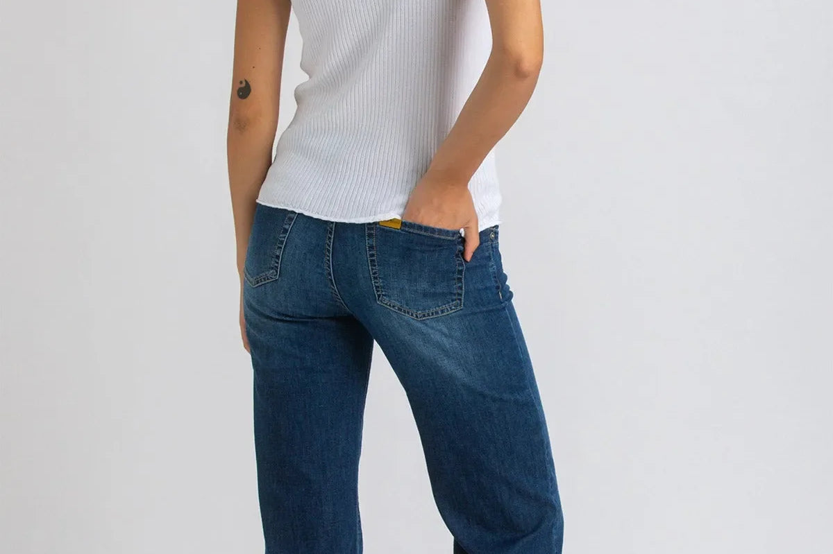Woman wearing white top and dark blue wide leg maternity jeans on white background