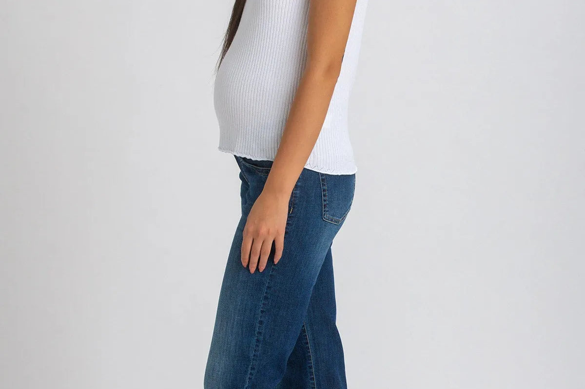 Woman wearing white top and dark blue wide leg maternity jeans on white background