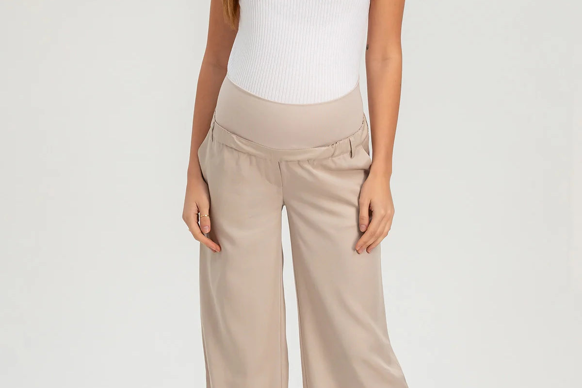 Woman wearing a white sleeveless top and beige wide-leg pants on a white background