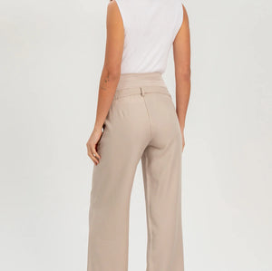 Woman wearing beige high-waisted pants and a white sleeveless top on a white background
