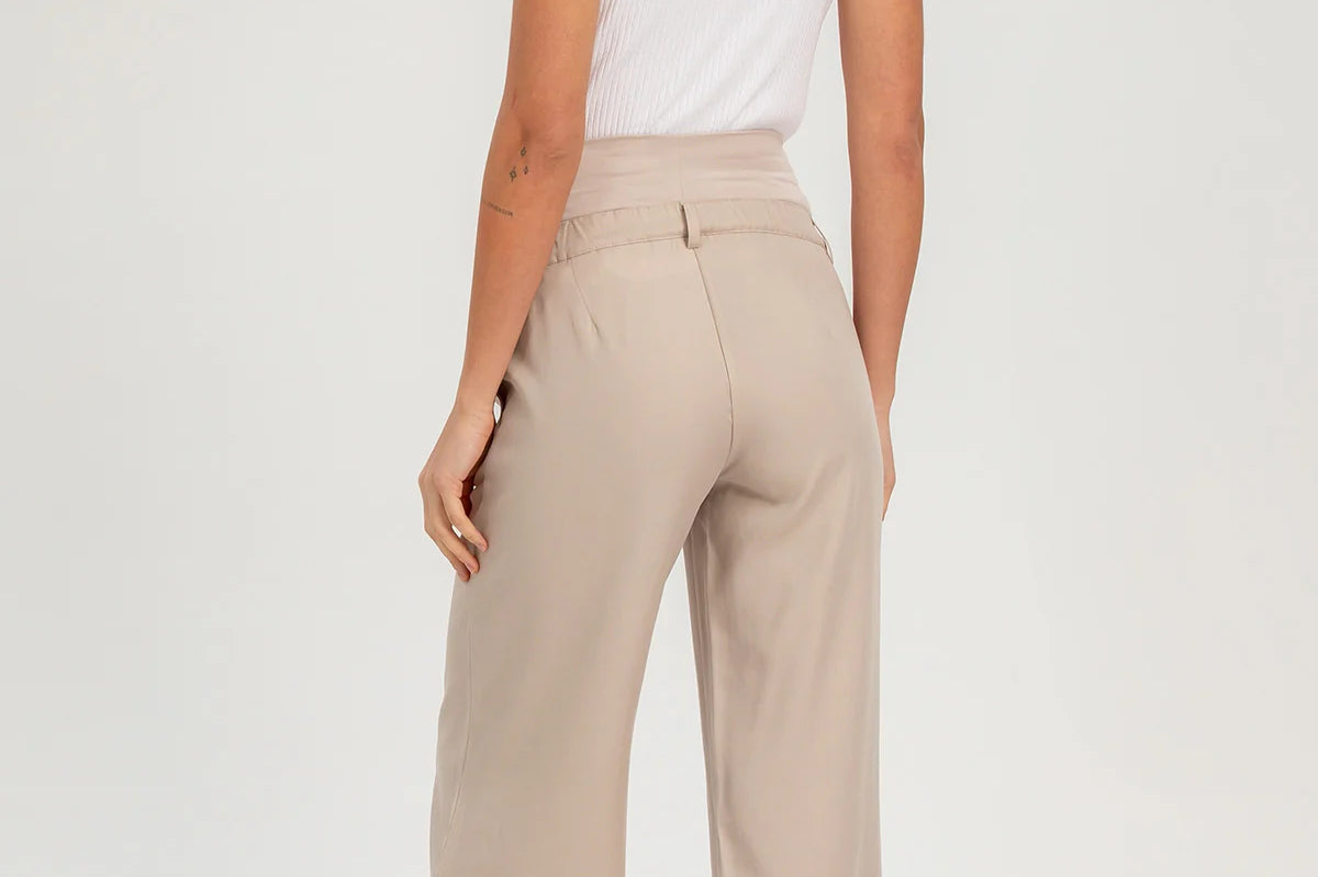 Woman wearing beige high-waisted pants and a white sleeveless top on a white background