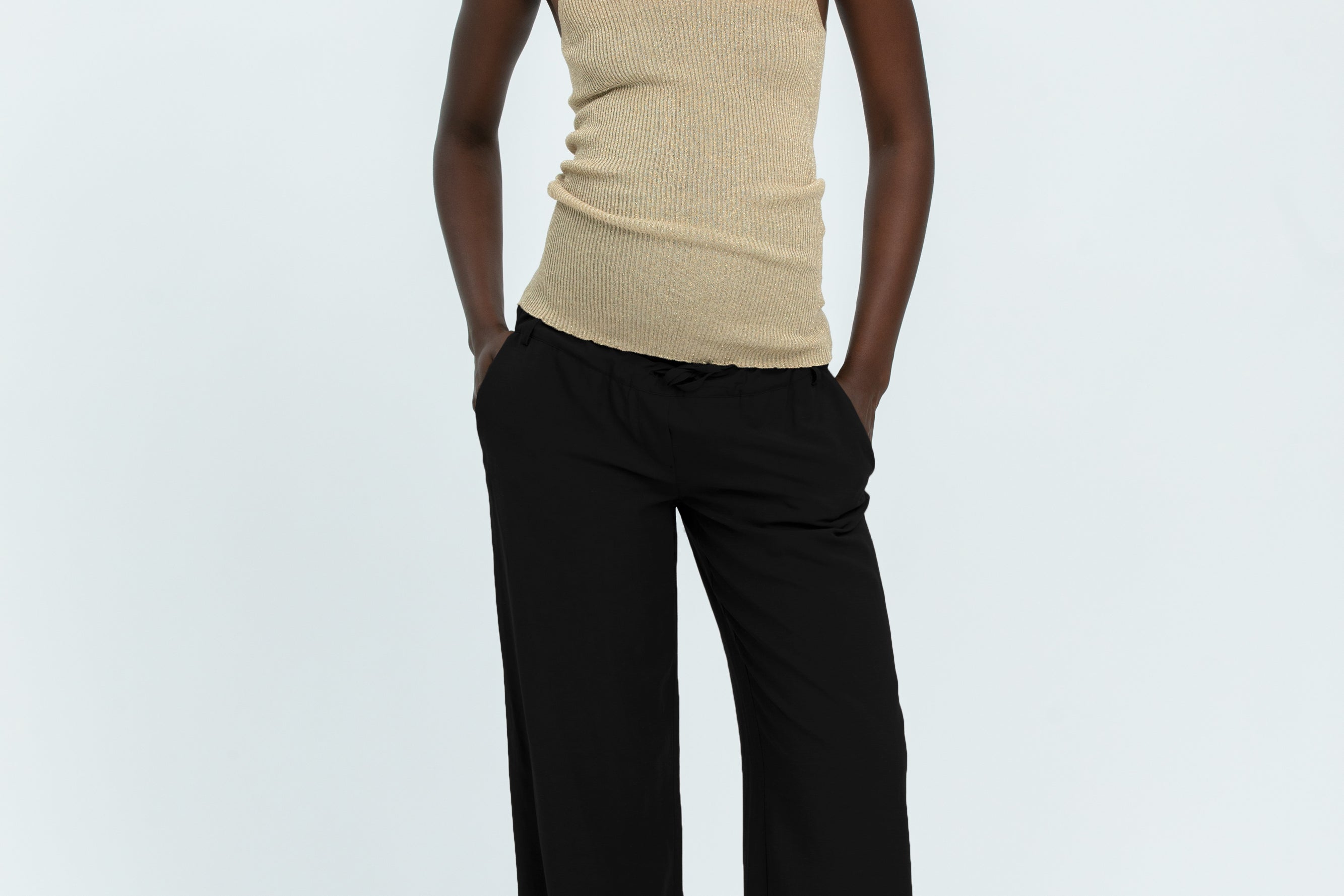 Woman wearing black linen trousers and beige vest top
