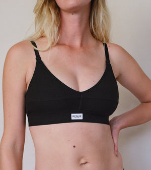 A woman wearing a black underwire bra with thin adjustable shoulder straps and a small white brand label on the front band. The brand name 'RENUE' is visible on the label.