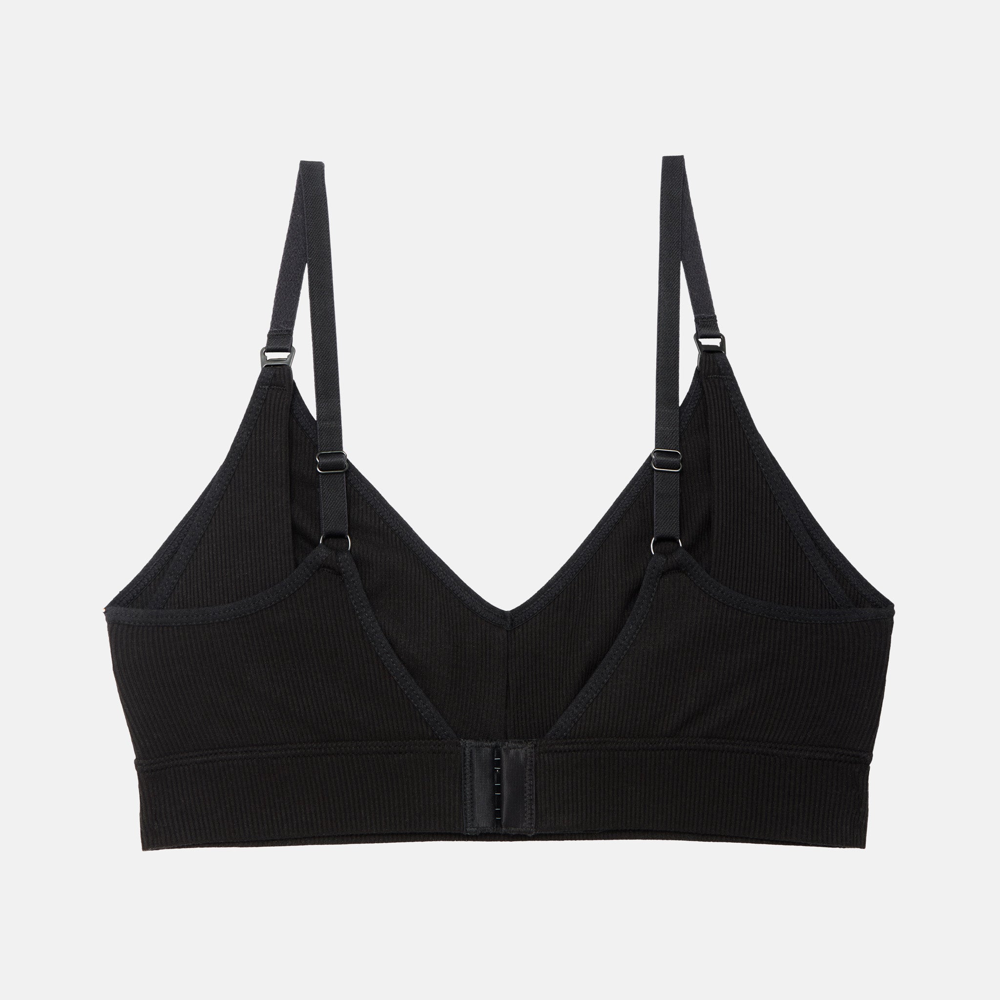 A black ribbed wireless bralette with adjustable shoulder straps and a central hook-and-eye closure, displayed against a light gray background.