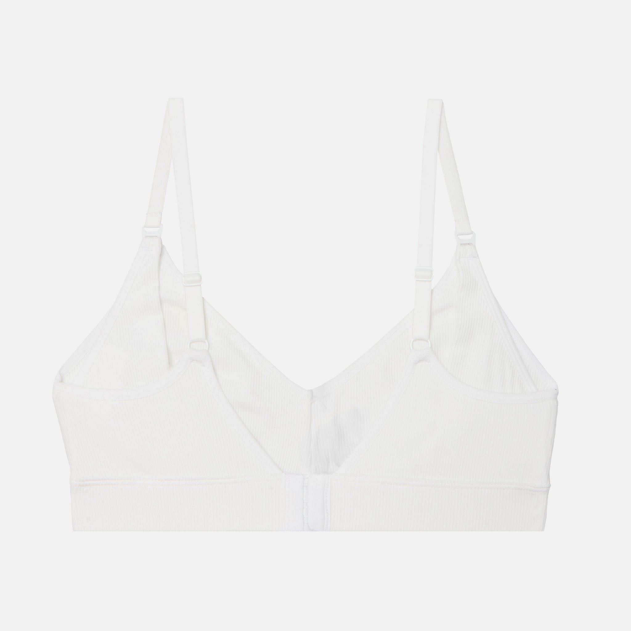 A white seamless bralette with adjustable shoulder straps and a center front closure, shown flat against a light gray background.
