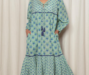 Woman wearing a green and blue patterned dress against a white curtain background