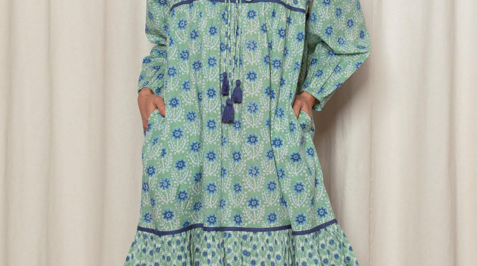 Woman wearing a green and blue patterned dress against a white curtain background