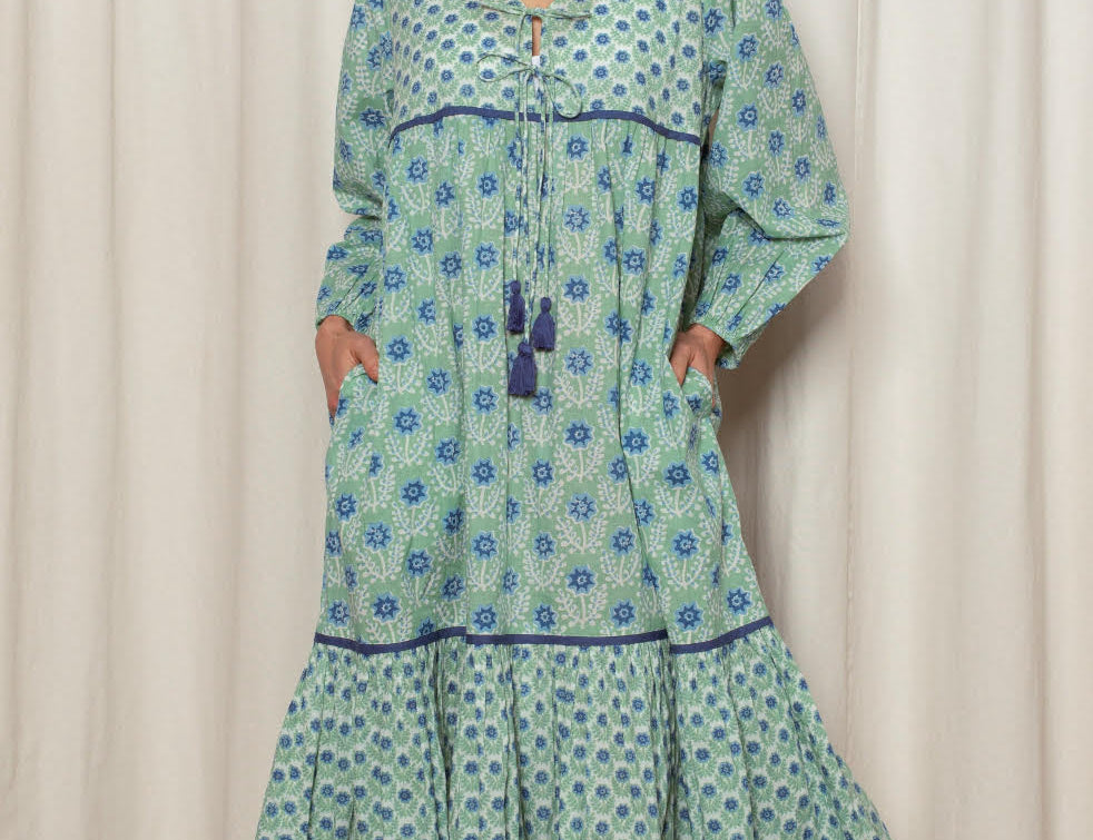 Woman wearing a green and blue patterned dress against a white curtain background