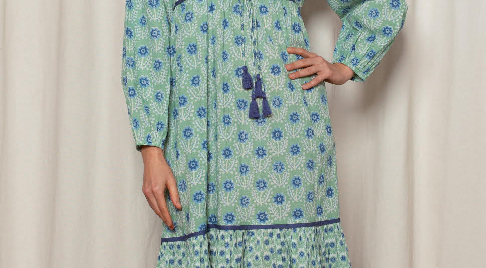Woman wearing a green patterned dress standing against a white curtain.