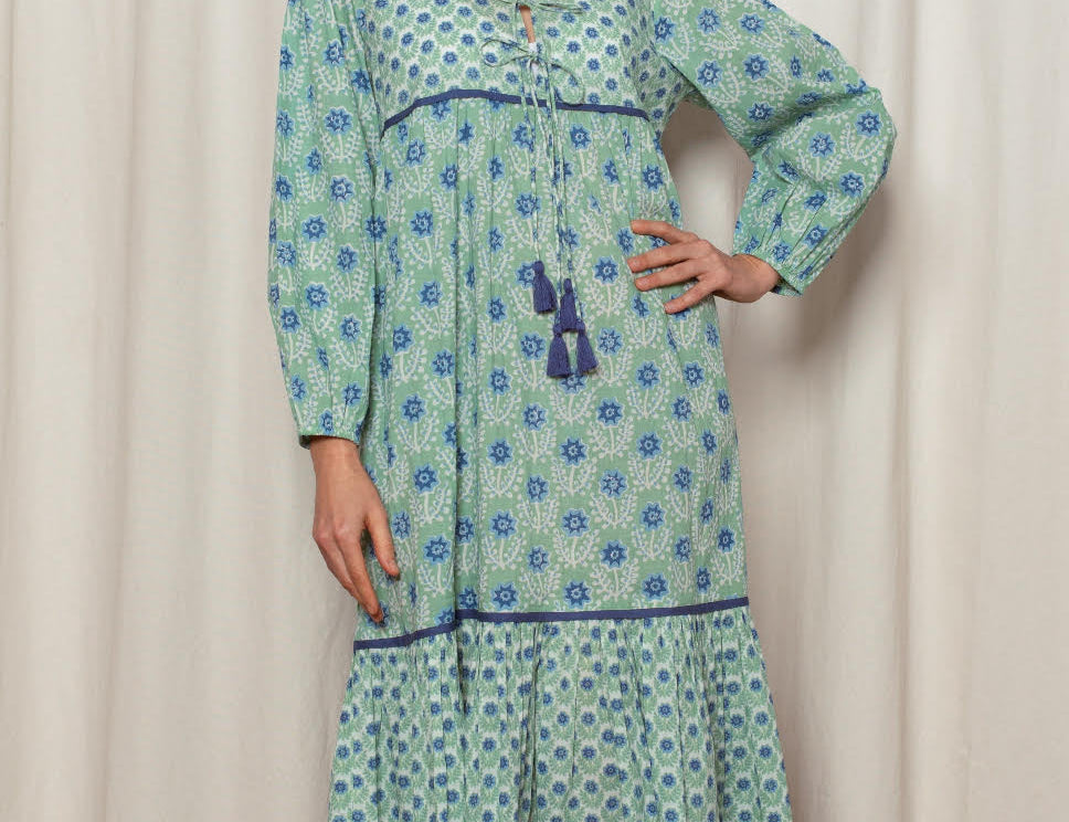 Woman wearing a green patterned dress standing against a white curtain.