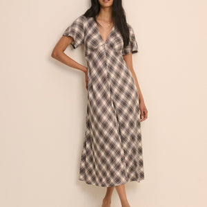 A woman modeling a short-sleeve midi dress with a brown, beige, and white plaid pattern against a plain beige studio background.