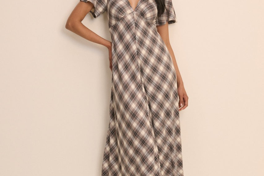 A woman modeling a short-sleeve midi dress with a brown, beige, and white plaid pattern against a plain beige studio background.