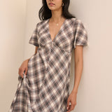A woman modeling a short-sleeve plaid midi dress with a wrap-style V-neckline, photographed against a plain beige wall.