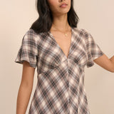 A woman wearing a short-sleeve plaid dress with a V-neckline, photographed against a plain beige studio background.