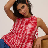 Woman wearing a red and white checkered top with floral patterns, sitting on a wooden surface.