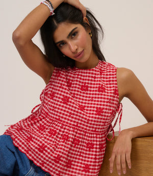 Woman wearing a red and white checkered top with floral patterns, sitting on a wooden surface.