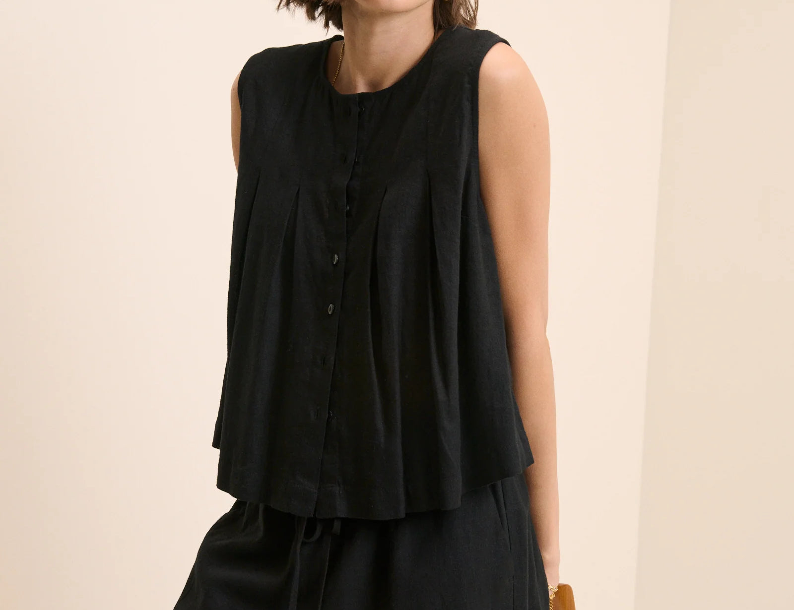 Woman wearing a black sleeveless dress against a beige background