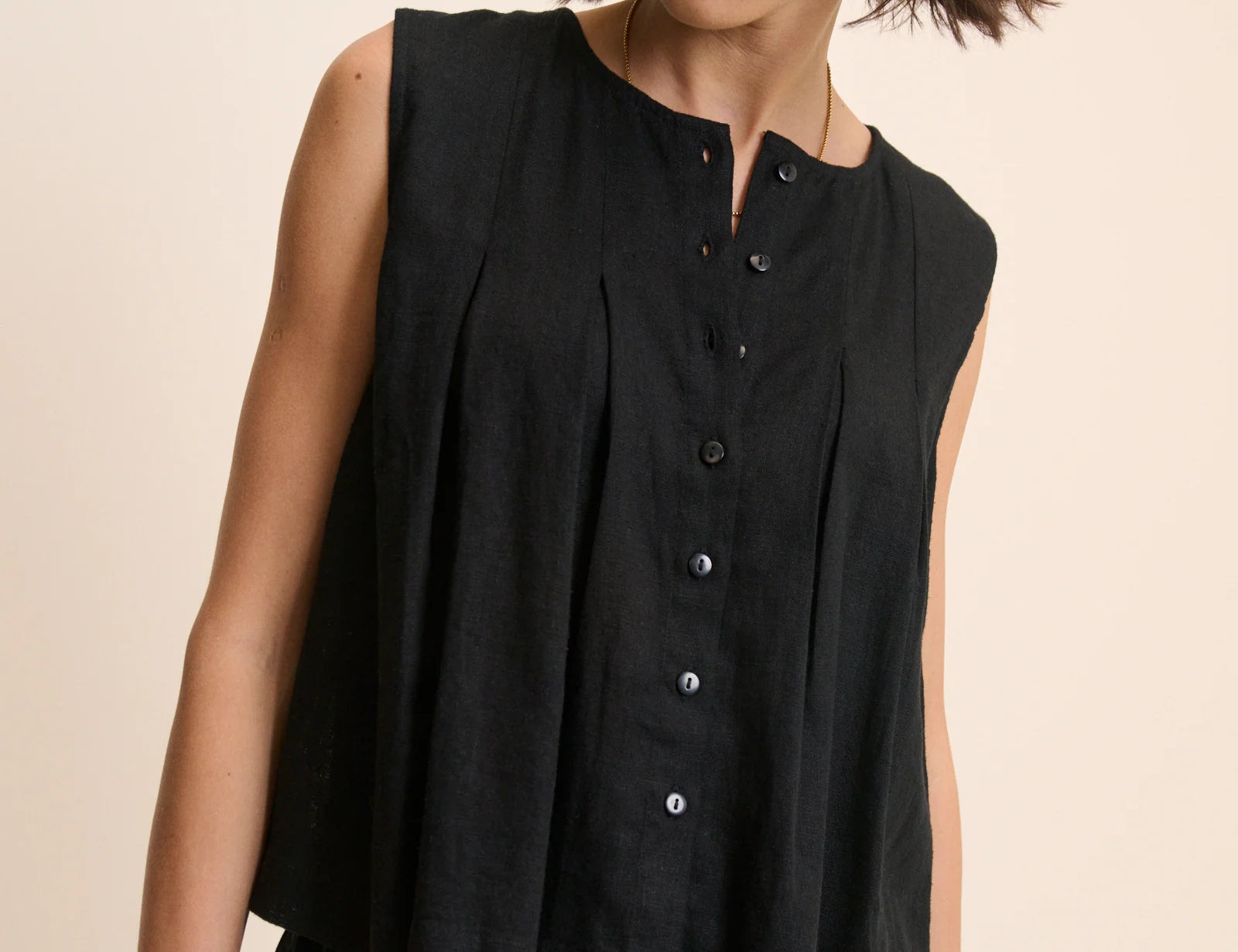 Woman wearing a black sleeveless top with buttons on a beige background