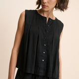 Woman wearing a black sleeveless top with buttons on a beige background