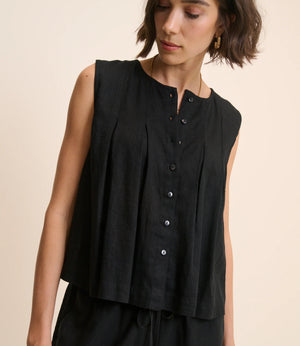 Woman wearing a black sleeveless top with buttons on a beige background