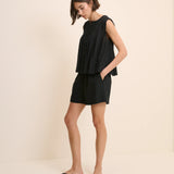 Woman wearing a black sleeveless top and shorts on a beige background