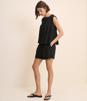 Woman wearing a black sleeveless top and shorts on a beige background