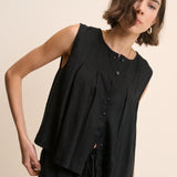 Woman wearing a black sleeveless top with buttons on a beige background