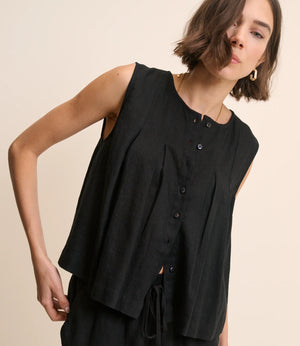 Woman wearing a black sleeveless top with buttons on a beige background