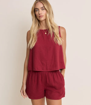 Woman wearing a red sleeveless top and shorts set against a beige background