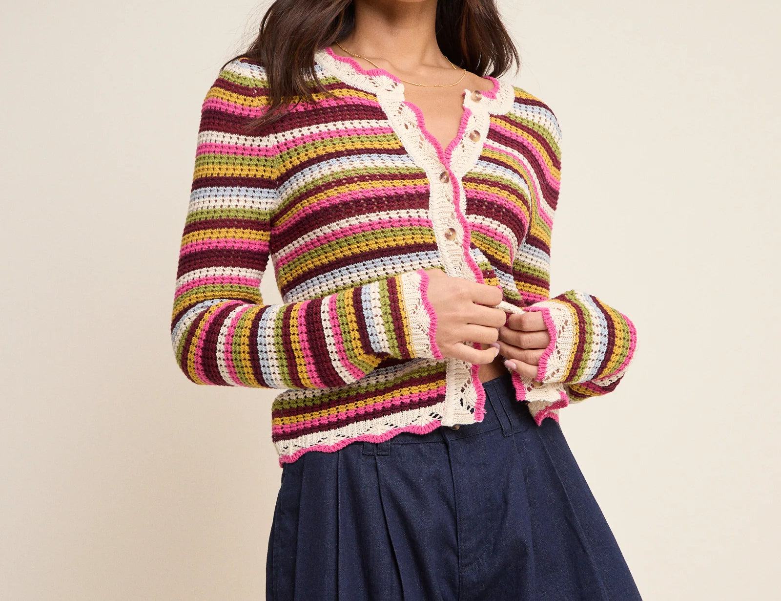 Woman wearing a colorful striped sweater and navy shorts on a beige background