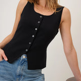 Woman wearing a black sleeveless top with buttons and blue jeans against a white background