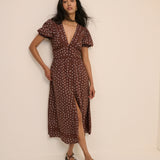 Woman wearing a brown dress with white patterns against a beige background