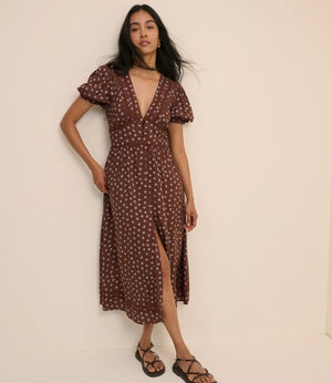 Woman wearing a brown dress with white patterns against a beige background