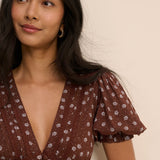 Woman wearing a brown floral dress against a beige background