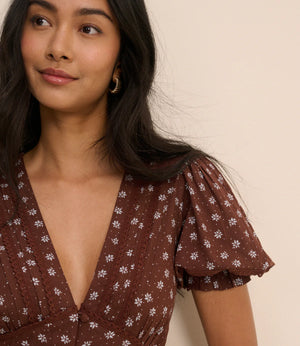 Woman wearing a brown floral dress against a beige background