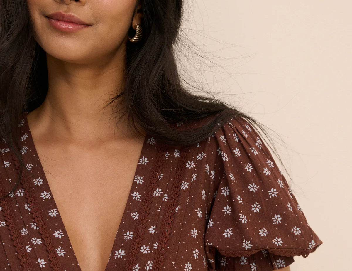Woman wearing a brown floral dress against a beige background