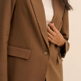 A close-up of a person wearing a camel brown blazer over a white top, with the hand adjusting the front button.