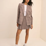 Woman wearing a plaid suit with a white shirt underneath on a beige background