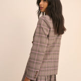 Woman wearing a plaid blazer and skirt set on a beige background