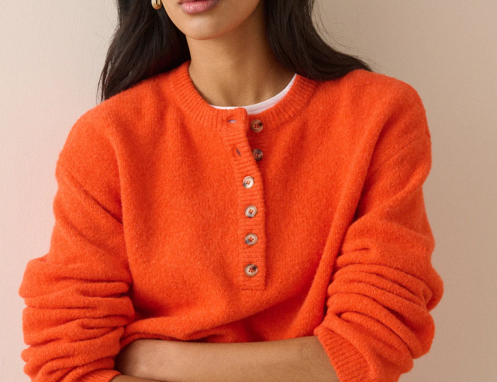 A woman wearing a bright orange fuzzy knit sweater with a buttoned henley-style neckline, photographed against a plain beige studio background.