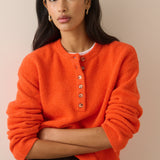 A woman wearing a bright orange fuzzy knit sweater with a buttoned henley-style neckline, photographed against a plain beige studio background.